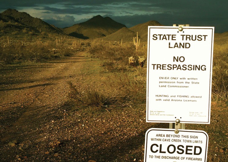 A sign states "State Trust Land, No Trespassing" along a road in Arizona.